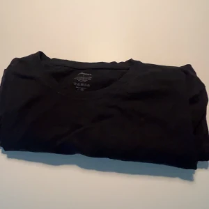 Svart t-shirt från Newbody i bomull - En klassisk svart t-shirt från Newbody i storlek L. T-shirten är tillverkad i 100% bomull, har rund hals och korta ärmar. Perfekt basic-plagg att ha i garderoben och lätt att matcha med allt.