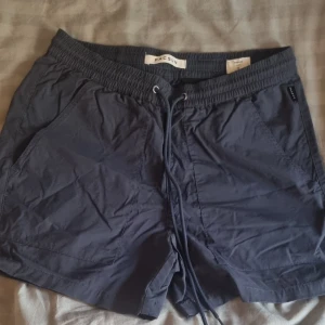 Mörkblå shorts från Pacsun med snörning - Snygga mörkblå shorts från Pacsun med elastisk midja och snörning framtill. Modellen har två sidofickor och två bakfickor, perfekt för chill dagar. Lätta och sköna, passar grymt till sommaren.