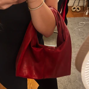 Röd axelväska från Gina Tricot - Säljer en snygg röd handväska från Gina Tricot. Väskan stängs med tryckknapp. Perfekt storlek för att få plats med allt du behöver och har en stilren, minimalistisk design.