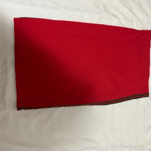 Röd långkjol med grön kant - En stilren röd långkjol med rak passform och en grön rand längs nederkanten. Kjolen har en enkel design som gör den lätt att matcha med olika toppar. Perfekt för dig som gillar färg och vill sticka ut lite extra.