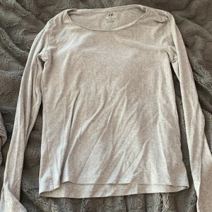 Ljusgrå ribbad långärmad tröja H&M - En basic ljusgrå långärmad tröja från H&M i ribbad ekologisk bomull. Tröjan har rund halsringning och en slim passform som sitter snyggt på kroppen. Perfekt att styla med jeans eller kjol för en enkel och clean look.