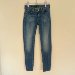 Blå skinny jeans från Lee - Storlek: W25 L31. Snygga blå skinny jeans från Lee med klassisk femficksdesign och guldfärgade detaljer. Jeansen har en smal passform, normal midja och är tillverkade i mjukt denimtyg. Perfekta för dig som gillar en stilren och enkel look. 