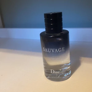 Dior Sauvage parfym 100ml - Dior Sauvage parfym i en stilren glasflaska med svart till transparent färgskiftning och svart kork. Flaskan rymmer 100 ml och har tydlig Dior-logga. En ikonisk doft med fräsch och maskulin känsla, perfekt för dig som gillar exklusiva parfymer.