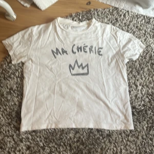 Vit t-shirt Ma Chérie Gina Tricot - Vit t-shirt från Gina Tricot med svart text 'Ma Chérie' och en krona tryckt på framsidan. Klassisk rund hals och korta ärmar. Tillverkad i mjuk bomull, perfekt för en chill och trendig look. 💕