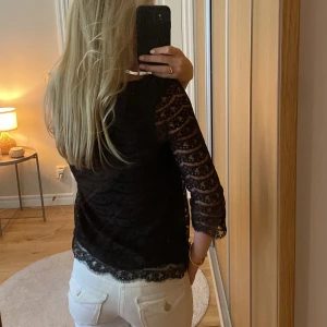 Svart spetsblus från Lindex XS - Svart blus från Lindex i storlek XS med snyggt spetsmönster och trekvartsärm. Blusen har rund halsringning och är genombruten i ärmarna för en extra fin look.