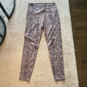 Lila snakeprint leggings från Aimn - Säljer ett par snygga leggings från Aimn i färgen dusty violet med coolt ormmönster. De är högmidjade och tillverkade i stretchigt material (73% polyester, 27% spandex) som sitter tajt och bekvämt. Perfekta för träning eller chill dagar.