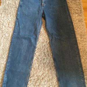 Blå relaxed jeans från H&M - Säljer ett par blå relaxed fit jeans från H&M. Klassisk femficksmodell med raka ben och normalhög midja. Jeansen är i bomull och har snygga kopparfärgade nitar och knapp. Perfekta för en chill och avslappnad stil.