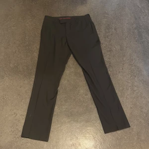 Svarta kostymbyxor med raka ben - Snygga svarta kostymbyxor från dressman med klassisk rak passform och pressveck. Byxorna har hällor för bälte, sidfickor och bakfickor med knappar. Perfekta för en clean och stilren look. Materialet känns mjukt och följsamt.