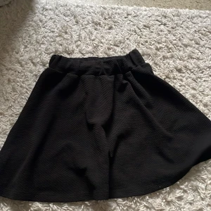 Svart kortkjol med struktur - En svart kortkjol med elastisk midja och lätt utställd passform. Väldigt basic och snygg, pris går att diskuteras, har inte använt på länge därför säljer jag