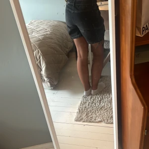 Svarta cargoshorts med snörning - Säljer ett par snygga svarta cargoshorts med vita kontrastsömmar och flera fickor på sidorna. Shortsen har hög midja, snörning i bensluten och är gjorda i jeansmaterial. Perfekta för en chill och trendig look i sommar.