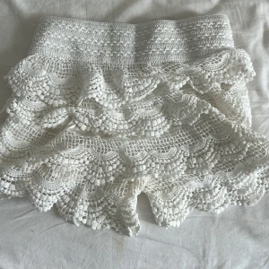 Vita virkade shorts med volang - Superfina vita virkade shorts med bred resår i midjan och flera lager volanger. De har en romantisk och bohemisk känsla med detaljerad spets och vågig kant. Perfekta för varma dagar när du vill sticka ut lite extra.