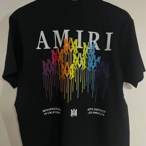 Svart AMIRI t-shirt med färggrafik - Svart t-shirt från AMIRI med stor vit logga och färgglad grafisk print i regnbågsfärger på bröstet och ryggen. T-shirten har klassisk passform, rund hals och är tillverkad i mjuk bomull. Perfekt statement-plagg för dig som gillar streetwear och färg.