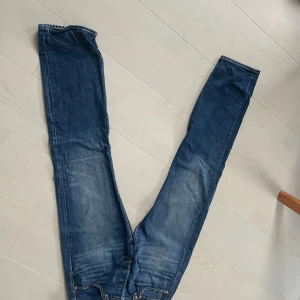 Levi's 501 blå jeans W31 L34 - Klassiska Levi's 501 jeans i blå denim med raka ben och normal passform. Snyggt slitna detaljer och ikoniska bakfickor med gul söm. Perfekta för dig som gillar tidlös stil och vill ha ett par jeans som alltid funkar.