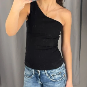 Svart oneshoulder topp - Snygg svart topp med oneshoulder-design. Tight passform som framhäver figuren. Perfekt för fest men även för en vanlig vardag, använd en gång innan, inte kommit till användning 