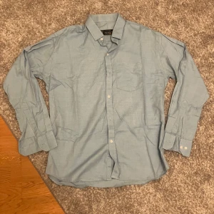 Ljusblå skjorta från Burberrys - Snygg ljusblå skjorta från Burberrys i klassisk modell med krage, bröstficka och knappar framtill. Skjortan är långärmad och tillverkad i bomull, perfekt för en clean och stilren look. Storlek 15 1/2 vilket motsvarar S-M