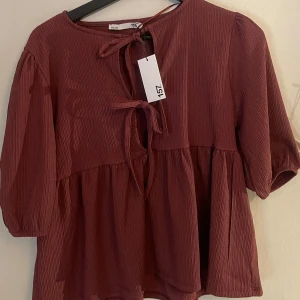 Vinröd blus med knyt från 157 - Vinröd blus med avslappnad passform och två knyt framtill. Blusen har trekvartsärmar med lätt puff! Helt ny! Storlek xs men är som en S 
