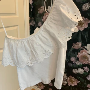 Vit omlottop från Zara med volang - Superfin vit topp från Zara med omlottkänsla och bred volang med broderade blommor. Ena axeln är bar.