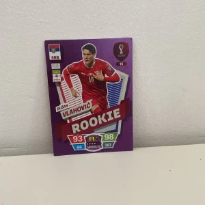 Rookie - Dušan Vlahović (FIFA World Cup Qatar 2022 Adrenalyn XL) - Samlar- och spelkort med Dušan Vlahović från FIFA World Cup Qatar 2022. Perfekt för dig som älskar fotboll, samlar på unika kort eller vill boosta din Adrenalyn XL-lek. Rookie-kortet har cool design och höga stats – ett måste för unga sportfans!