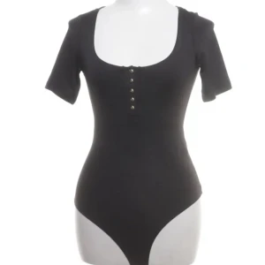 Svart body med knappar - Svart body med korta ärmar och djup rundad ringning framtill.  Jätte snygg och passar till alla tillfällen! Köpt från Sellpy (nyskick) men gilla inte hur den satt så säljer vidare. Hör av dig vid frågor💕
