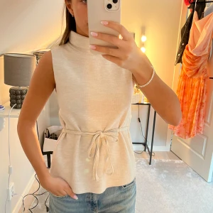 Topp - Snygg beige ärmlös topp med hög krage och knytband i midjan