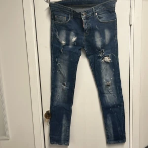 Blå slitna jeans från Dsquared2 - Säljer ett par blå jeans från Dsquared2 med slitningar och hål på flera ställen. Jeansen har klassisk femficksdesign, smal passform och tydliga slitdetaljer framtill. Perfekta för dig som gillar en edgy streetstil.