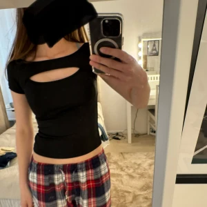 Svart croppad topp med cut-out - Säljer en svart croppad topp med korta ärmar och en snygg cut-out detalj vid bröstet. Toppen har tight passform och är perfekt för att skapa en trendig look.