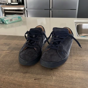 Svarta sneakers i mocka med snörning - Snygga svarta sneakers i mocka med klassisk design och svarta skosnören. Skorna har rund tå och platt sula, samt en brun insida som ger en schysst kontrast. Perfekta för en stilren vardagslook.