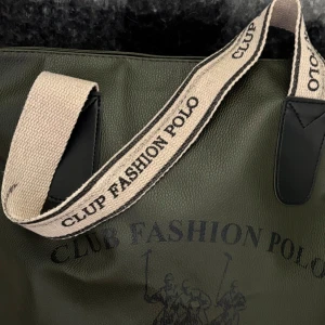 Club Polo - Stilren grön axelväska i syntetmaterial från Club Fashion Polo. Väskan har ljusa, breda axelband med tryckt logga och dragkedja upptill. Perfekt för att bära.