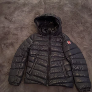 Mörkblå pufferjacka med luva från Colmar - Säljer en svart pufferjacka från Colmar med huva och dragkedja. På baksidan av jackan nere i hörnet vid colmar märket så är det ett litet jack som är ca 2 cm. Pris kan diskuteras.