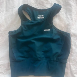 Mörkgrön sporttopp från Stronger - Säljer en mörkgrön sporttopp från Stronger med brottarrygg. Toppen är tight och har en sportig design, perfekt för träning. Materialet är syntet och ger bra stöd.