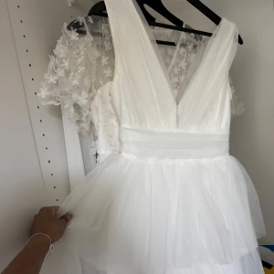 Perfekta studentklänningen - Säljer en vit klänning med flera lager tyll och djup v-ringning både fram och bak. Klänningen har breda axelband och markerad midja med ett band. Perfekt för speciella tillfällen. Den är från Gina Tricot