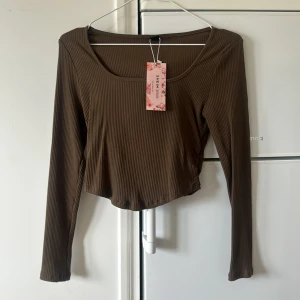 Brun ribbad croppad topp från SHEIN - Säljer en brun långärmad croppad topp från SHEIN. Toppen är ribbad och har en rundad, lite djupare halsringning. Perfekt att styla med jeans eller kjol för en trendig look.