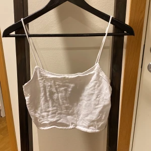 Vit linnetopp från FB Sister - Säljer en enkel och stilren vit linnetopp från FB Sister i storlek M. Toppen har tunna axelband och är tillverkad i ett lätt material, perfekt för varma dagar eller som lager under andra plagg.