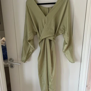 Ljusgrön omlottklänning med knytband - Säljer en ljusgrön långklänning med omlott-design och knytband i midjan. Klänningen har långa ärmar och en v-ringad framdel. Perfekt för dig som gillar en elegant och avslappnad stil.