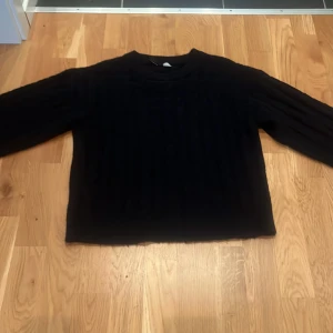 Svart kabelstickad tröja - Mysig svart kabelstickad tröja med rund hals och långa ärmar. Tröjan har en klassisk kabelstickad struktur och ribbade muddar vid ärmslut. Använt ett fåtal gånger och köpt för 249kr ordinalpris. Passar en xs då den är lite stor i storleken. 