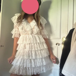 Vit spetsklänning med volanger från By Malina - Supersöt vit kortklänning från By Malina med flera lager volanger och v-ringning. Perfekt till tex student/ midsommar. Säljer pga köpte förra året och den kommer ej till användning längre! Är en tjej som brukar ha s/m och denna sitter bra på mig💕