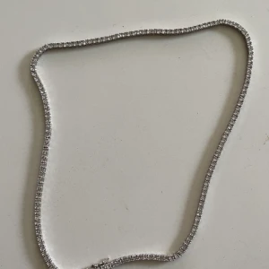 Silverfärgat tennisarmband med glittrande stenar - Ett stilrent och elegant tennisarmband i silverfärg med små glittrande stenar längs hela bandet. Perfekt för att addera lite extra bling till din outfit.
