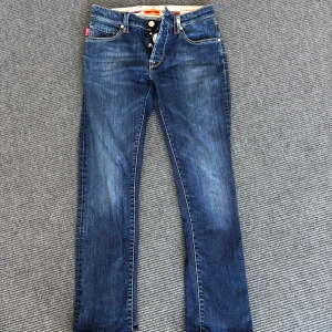 Blå jeans från Tramarossa - Snygga blå jeans från Tramarossa med klassisk femficksdesign och knappar i gylfen. Jeansen har kontrastsömmar och detaljer i rött på insidan. Perfekta för dig som gillar stilrena och tidlösa jeans.