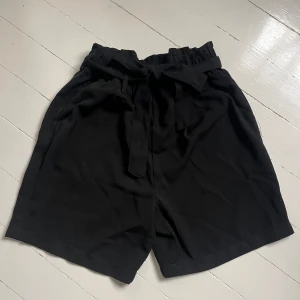 Svarta shorts med knytband - Svarta shorts med hög midja och knytband i midjan. De har en lös passform och är tillverkade i ett mjukt, lätt tyg som ger en avslappnad känsla. Perfekta för varma dagar och enkla att matcha med olika toppar. Skriv för fler bilder💞