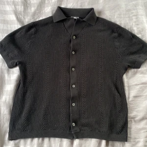 Svart stickad skjorta  - Säljer en svart stickad skjorta från H&M med korta ärmar och knappar framtill. Skjortan har en klassisk krage och ribbad struktur som ger en snygg och modern look. Perfekt för dig som gillar stilrena plagg. Priset kan sänkas vid snabb affär och vid ytligare fågor är de bara att höra av dig. Mvh Oliver 
