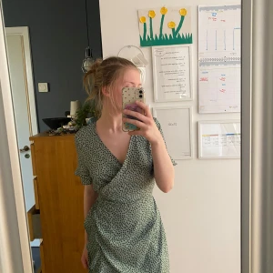 Grön omlottklänning med prickigt mönster - Säljer en ljusgrön omlottklänning med svarta prickar. Klänningen har korta ärmar, v-ringning och knyt i midjan. Perfekt för vår och sommar, och ger en fräsch och trendig look. Passar som M💗