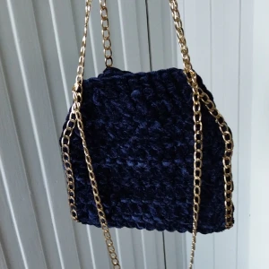 Mörkblå virkad väska med kedja - Säljer en snygg mörkblå väska med virkad struktur och guldfärgad kedja. Perfekt för att lyfta din outfit med en trendig accessoar. Väskan har en mjuk och fluffig känsla och passar till många tillfällen.