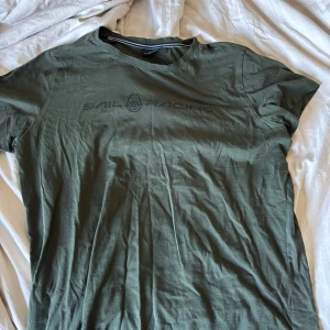Olivgrön t-shirt från Sail Racing - Säljer en olivgrön t-shirt från Sail Racing med tryckt logga över bröstet. T-shirten har rund hals och korta ärmar. Perfekt för en avslappnad stil.