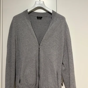 Grå kofta från Massimo Dutti - Stilren grå kofta från Massimo Dutti med dragkedja framtill. Tillverkad i en mjuk blandning av bomull och ull, perfekt för lager-på-lager. Ribbstickad krage och muddar ger en klassisk look. 😃