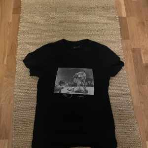 Svart t-shirt  - Svart t-shirt från Culture Kings med ett stort svartvitt tryck på framsidan som visar en klassisk boxningsscen. T-shirten har rund hals och korta ärmar. Perfekt för dig som gillar sportiga och stilrena plagg.