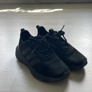 Svarta Adidas sneakers med mesh-ovandel - Säljer ett par helsvarta Adidas sneakers med klassiska tre ränder på sidan. Skorna har en ovandel i mesh, snörning och en tjock, platt sula för extra komfort. Perfekta för vardagsbruk eller träning.