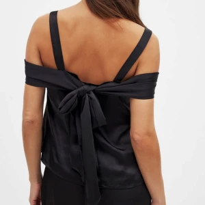 Svart satintopp med rosettdetalj från NA-KD - Säljer en svart satintopp från NA-KD. Toppen har en offshoulder-look💗💗