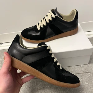 Maison margiela gats - Säljer ett par stilrena svarta maison margiela gats med vita snören och ljusbrun gummisula. Skorna har en klassisk design med rund tå och platt sula, perfekta för en clean och tidlös look. Skorna är använda ett fåtal gånger och säljer då de tyvärr inte passade mig. Hör av er vid minsta lilla fråga. Pris går att diskutera. 