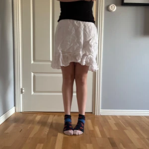 Vit volangkjol - Säljer en söt vit kjol med volangkant. Kjolen är kort och har en luftig känsla, perfekt för varma dagar. Passformen är normal och materialet känns lätt och bekvämt. det är ett resårband bak så den är lite stretchig men tajt där framme. Storlek 38 sitter som en vanlig 38