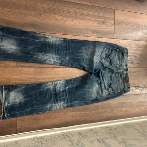 Blå jeans  - Säljer ett par blå jeans med slitna detaljer och ljusa partier. Klassisk femficksmodell med raka ben och låg midja. 